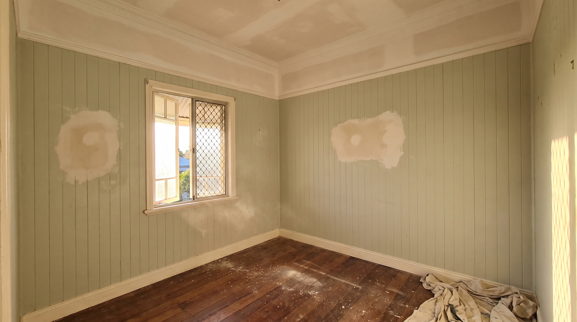 An empty Queenslander bedroom with the ceiling set and two patched sections on the board walls