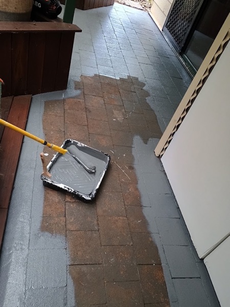 A roller and paint tray on a paved verandah part way through a coat
