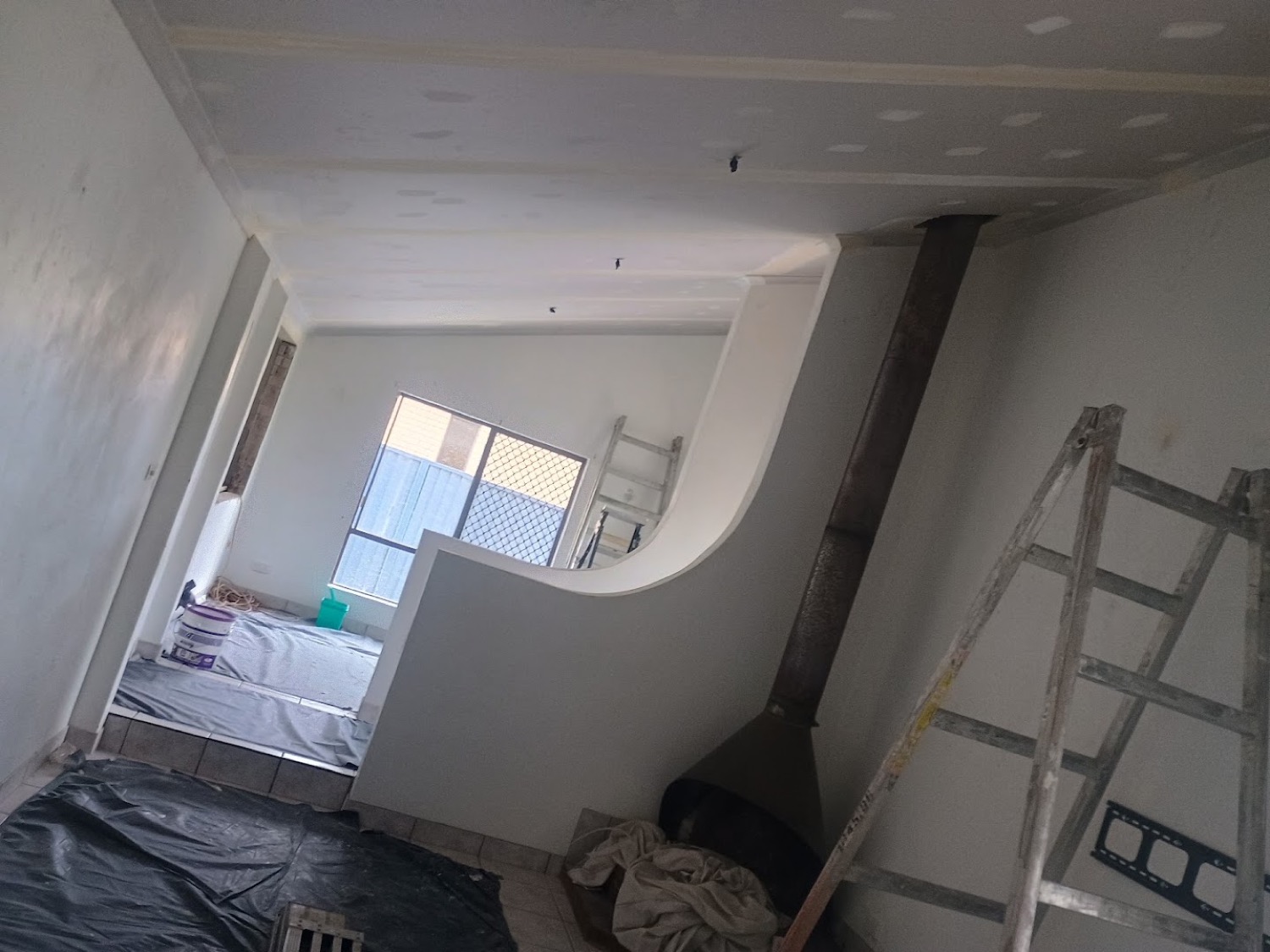 A set gyprock ceiling and curved bulkhead in a Bundaberg home, with a ladder and drop sheets in the room